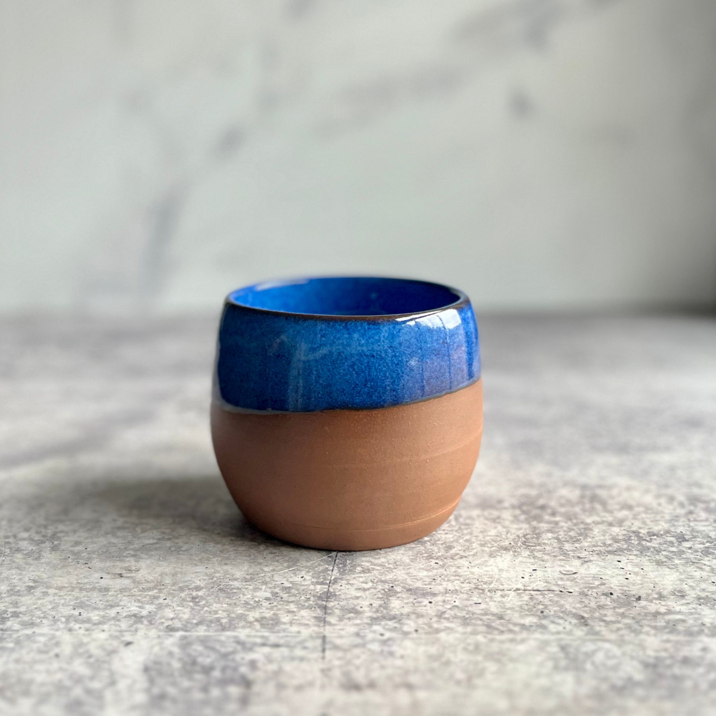 Handmade Blue stoneware stemless wine cup with half-glaze design and natural clay base, wheel-thrown at End of the Road Farm Studio Alabama.