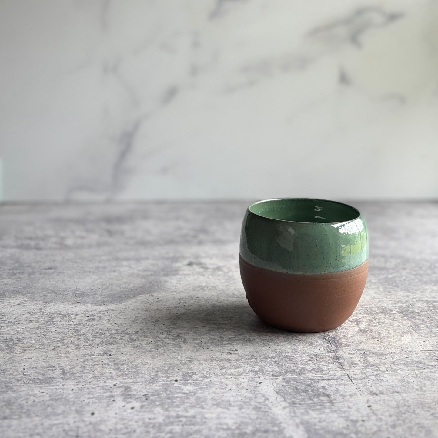 Handmade 12 oz green stoneware stemless wine cup with half-glaze design and natural clay base, wheel-thrown at End of the Road Farm Studio Alabama.