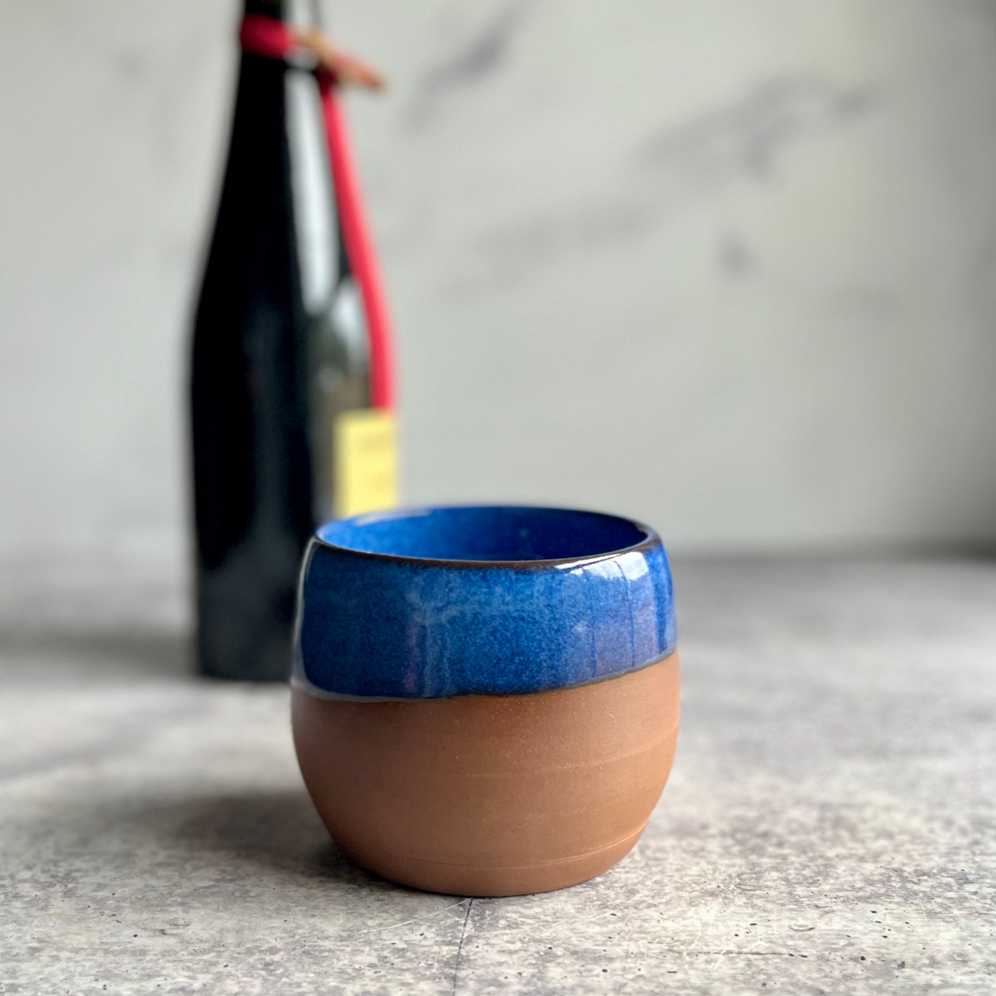 Handmade 12 oz Blue stoneware stemless wine cup with half-glaze design and natural clay base, wheel-thrown at End of the Road Farm Studio Alabama.