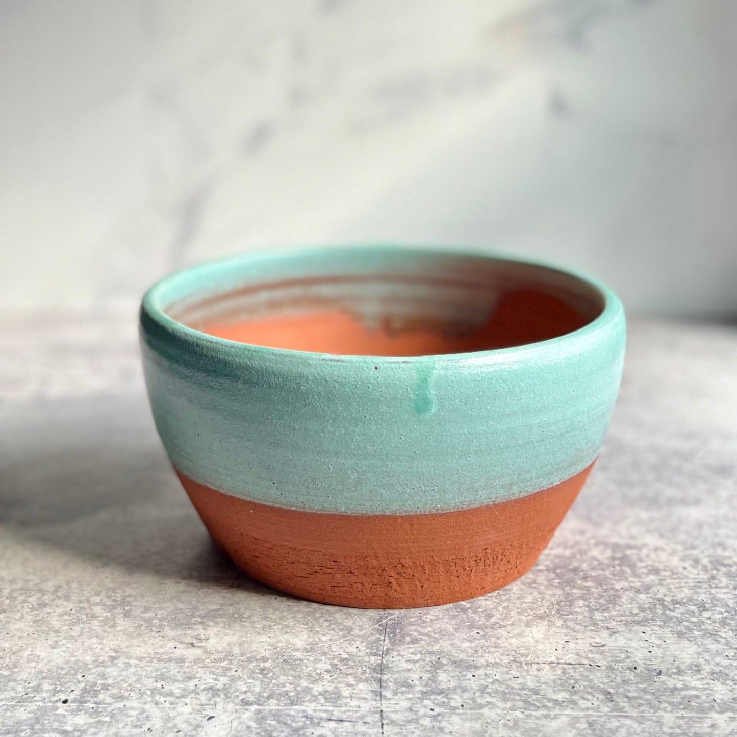 Medium earthenware ceramic planter glazed turquoise on top, on a gray surface.