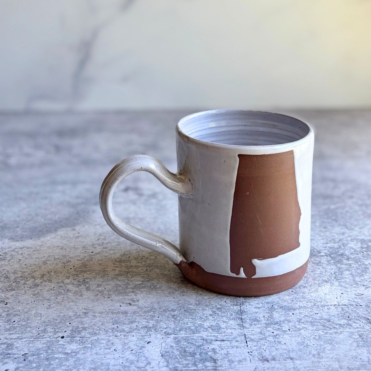 Handmade white stoneware coffee mug with Alabama state silhouette in natural clay, wax resist technique, wheel-thrown in Ethelsville Alabama