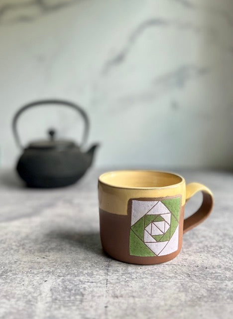 Ceramic mug with geometric design on a marble surface with a teapot in the background