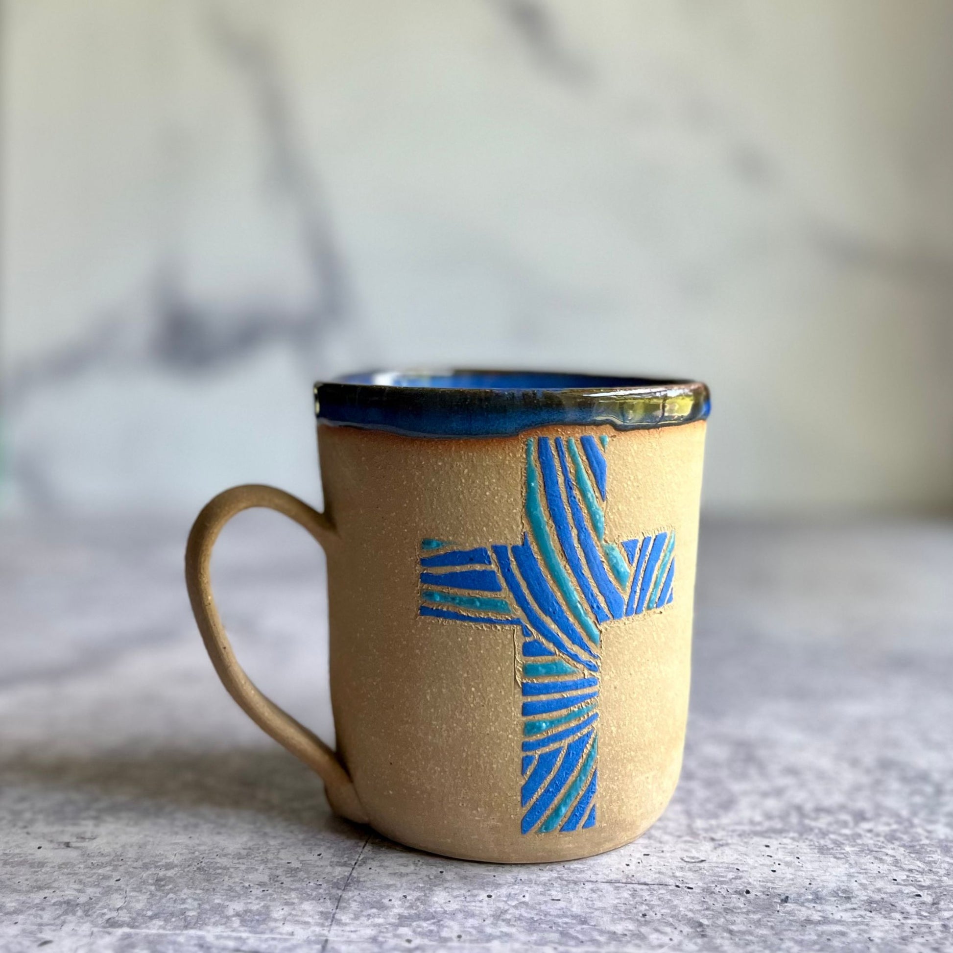 Ceramic mug with blue cross design on a neutral background