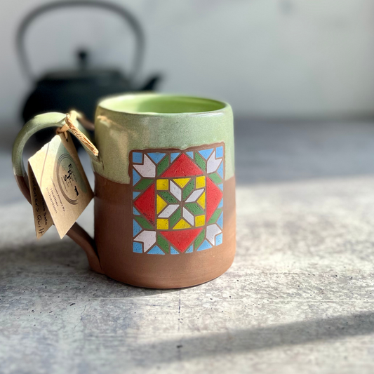 Green ceramic mug with a colorful geometric pattern on a gray surface