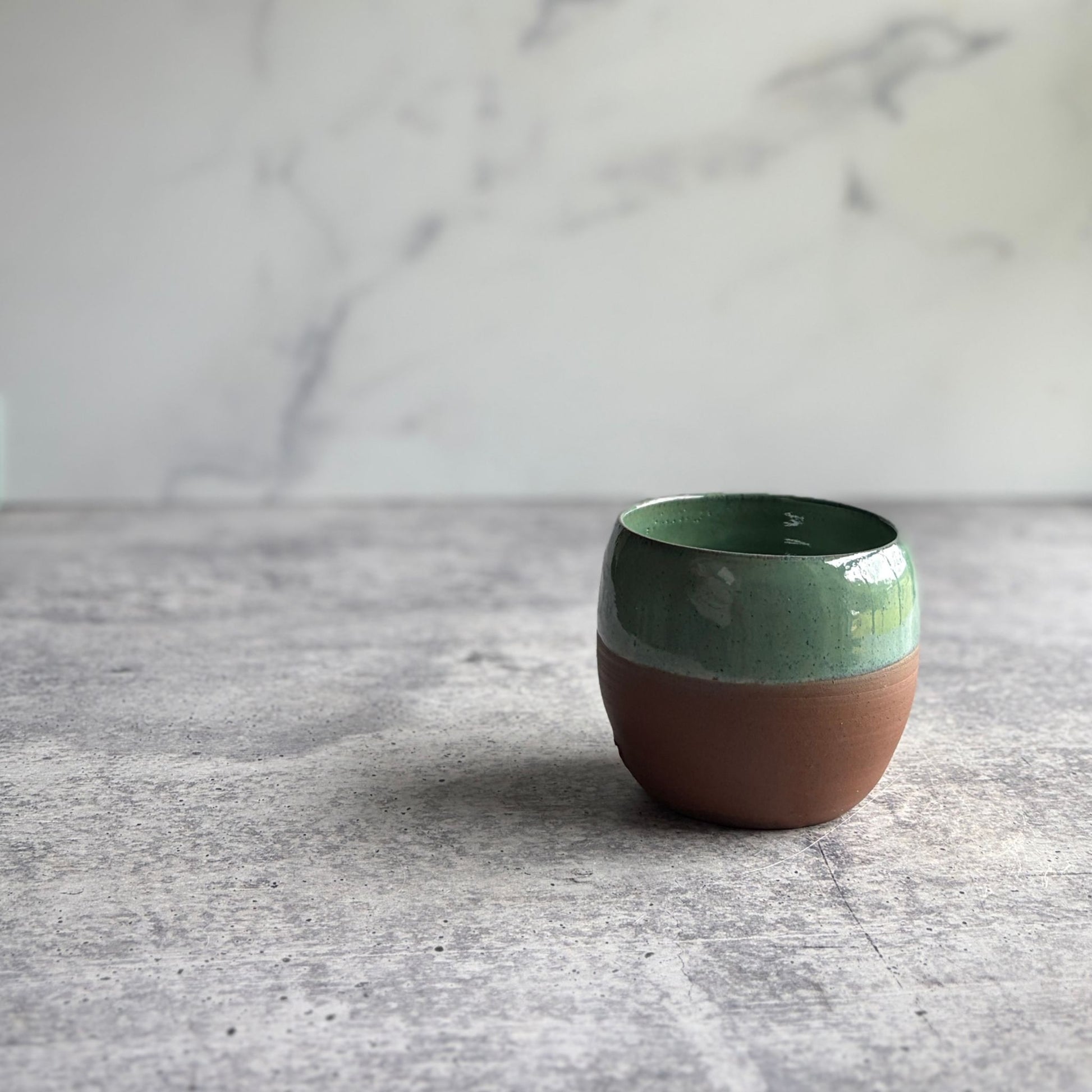Handmade 12 oz green stoneware stemless wine cup with half-glaze design and natural clay base, wheel-thrown at End of the Road Farm Studio Alabama.