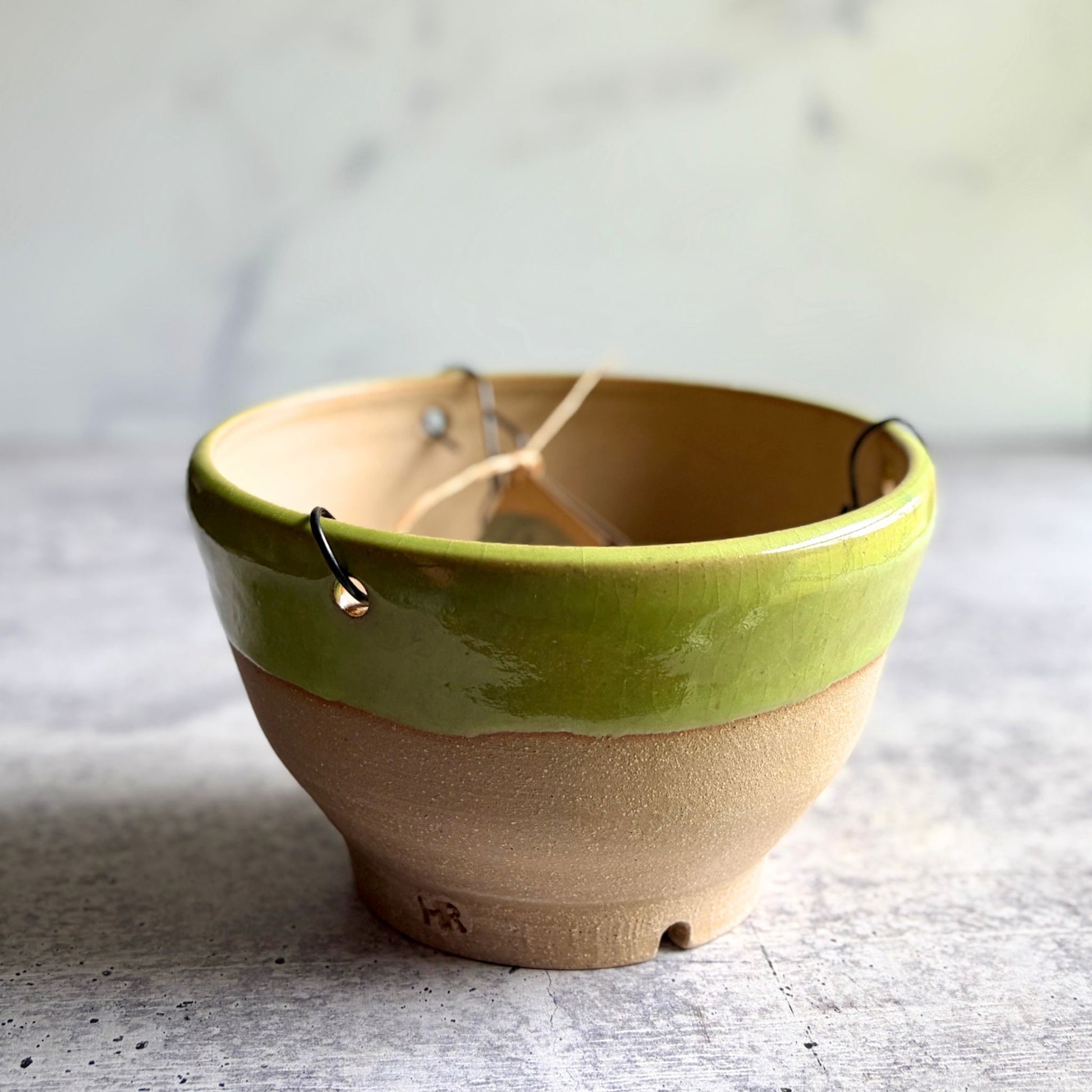 Side view of handmade lime green stoneware hanging planter, wheel-thrown at End of the Road Farm Studio Ethelsville Alabama, showing natural clay base and drainage hole