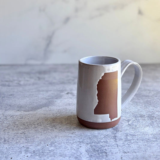 Handmade white stoneware coffee mug with Mississippi state silhouette in natural clay, wax resist technique, wheel-thrown in Ethelsville Alabama