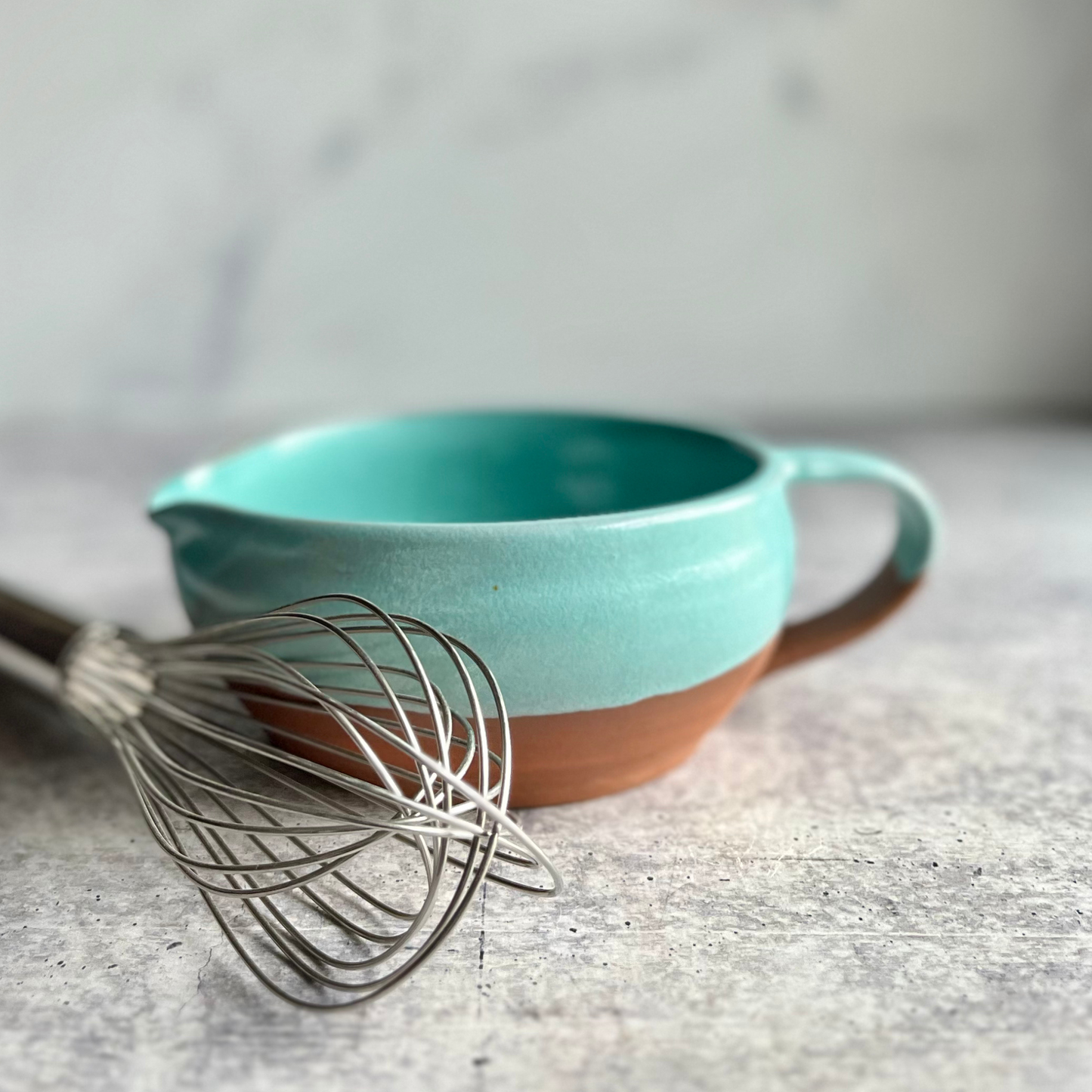 Turquoise and brown ceramic mixing bowl with a whisk on a gray surface