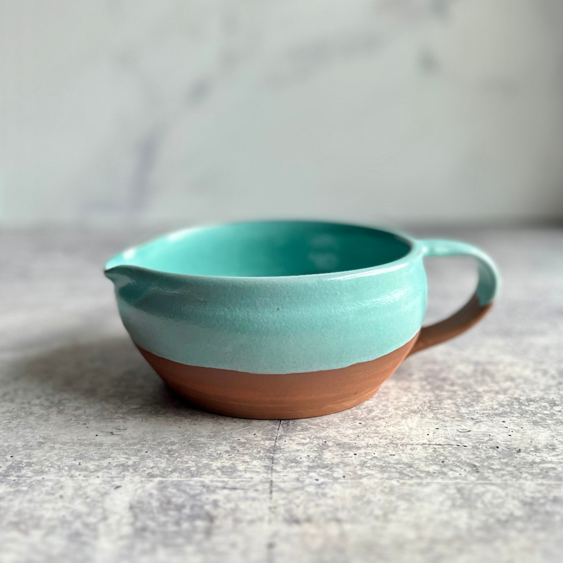Turquoise and brown ceramic mixing bowl on a gray surface with a blurred background