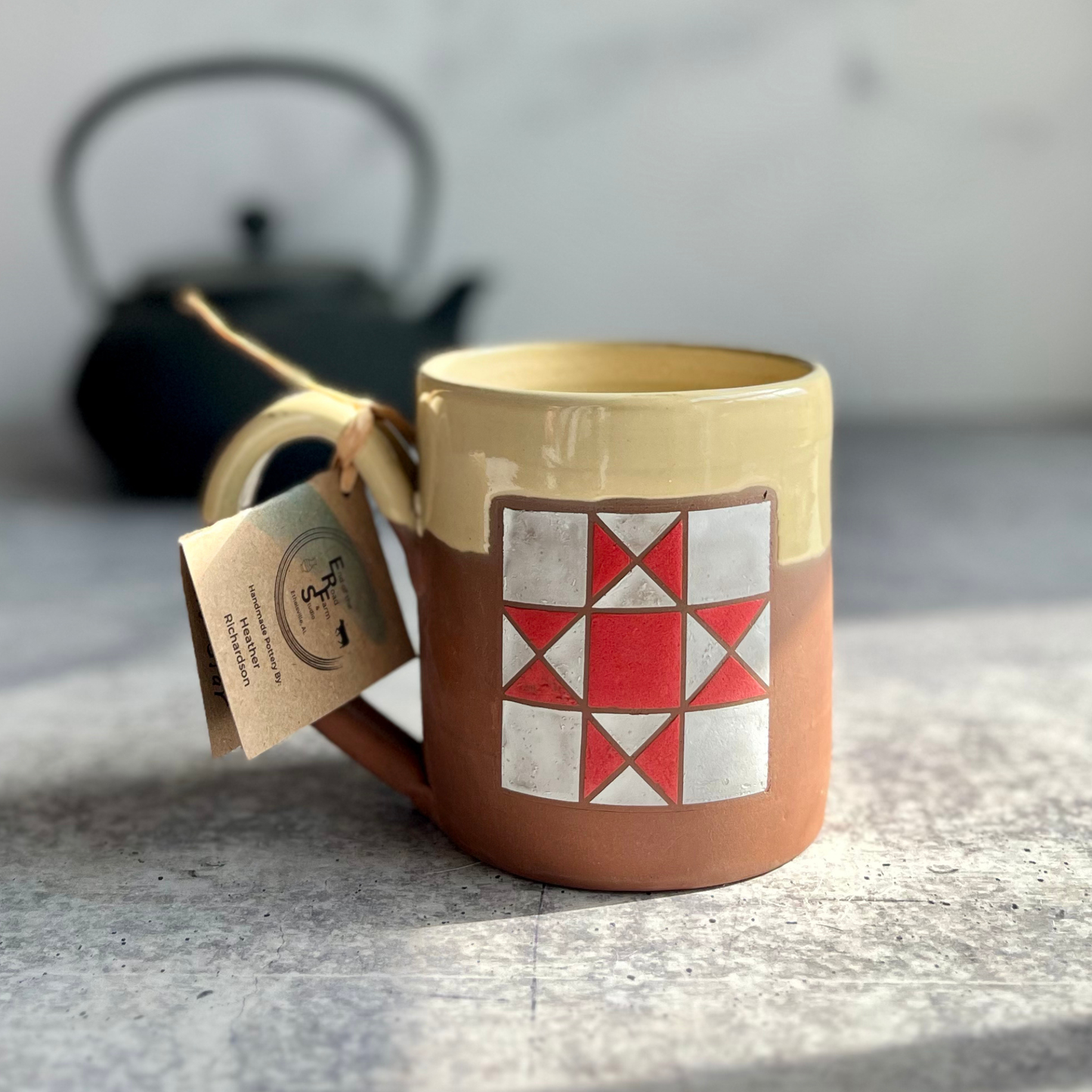 Ceramic mug with geometric design and a teapot in the background