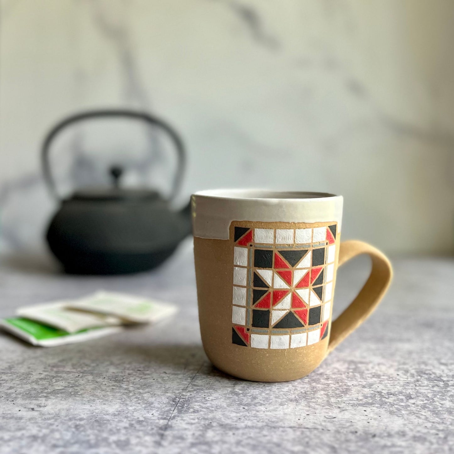Mug with geometric pattern on a table with a teapot and tea bags in the background