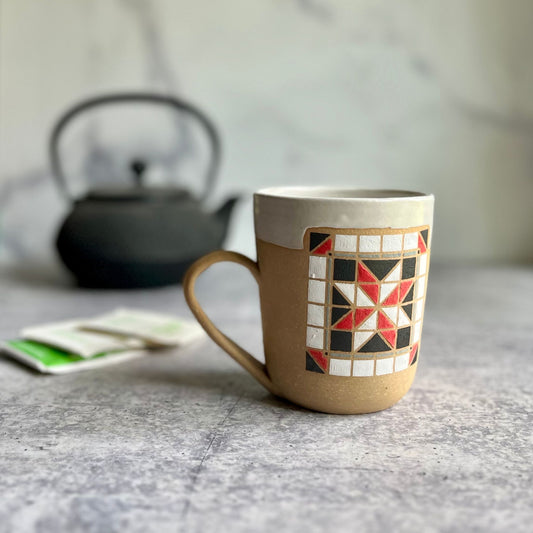Ceramic mug with geometric pattern on a marble surface, with a teapot in the background.