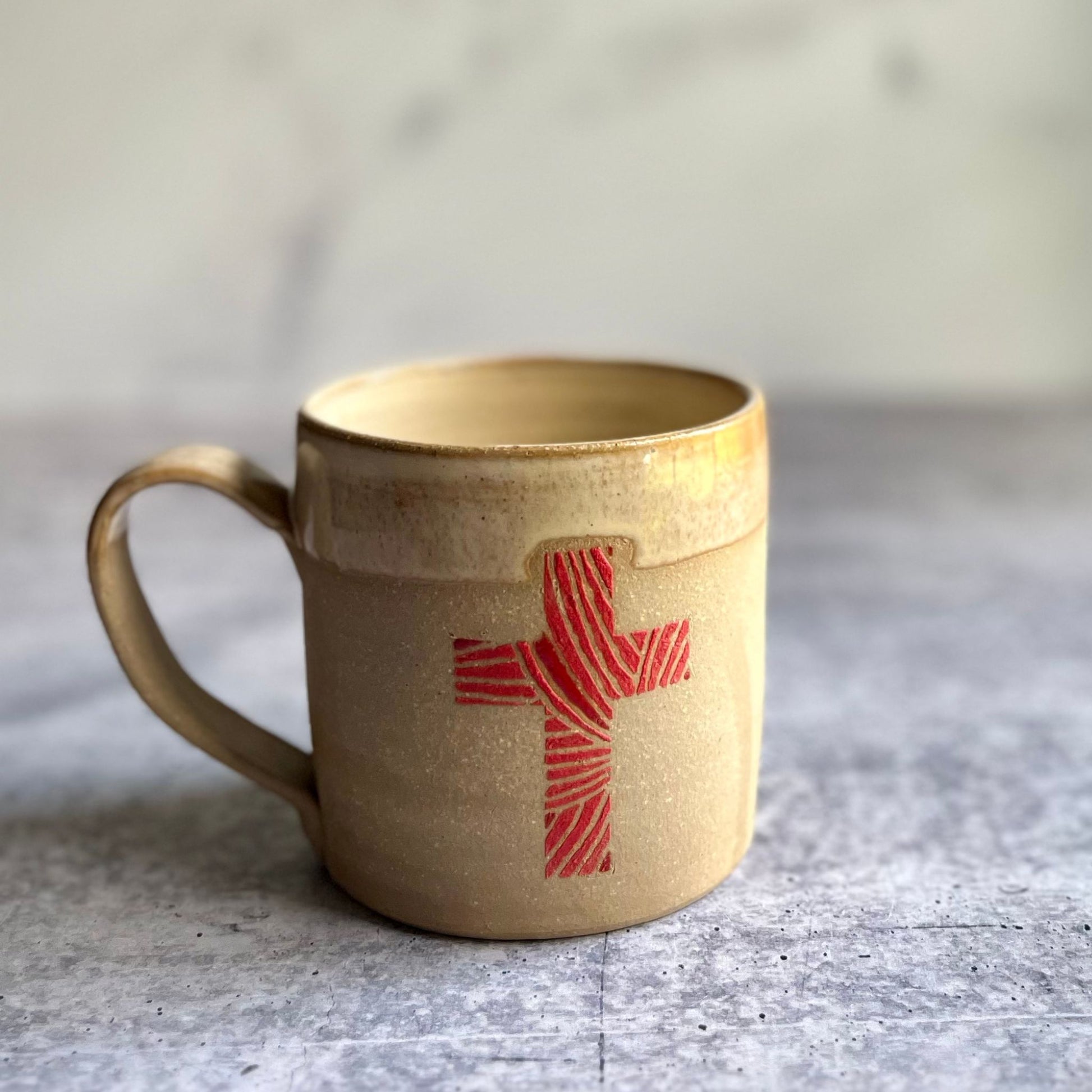 Brown ceramic mug with a red cross design on a gray surface