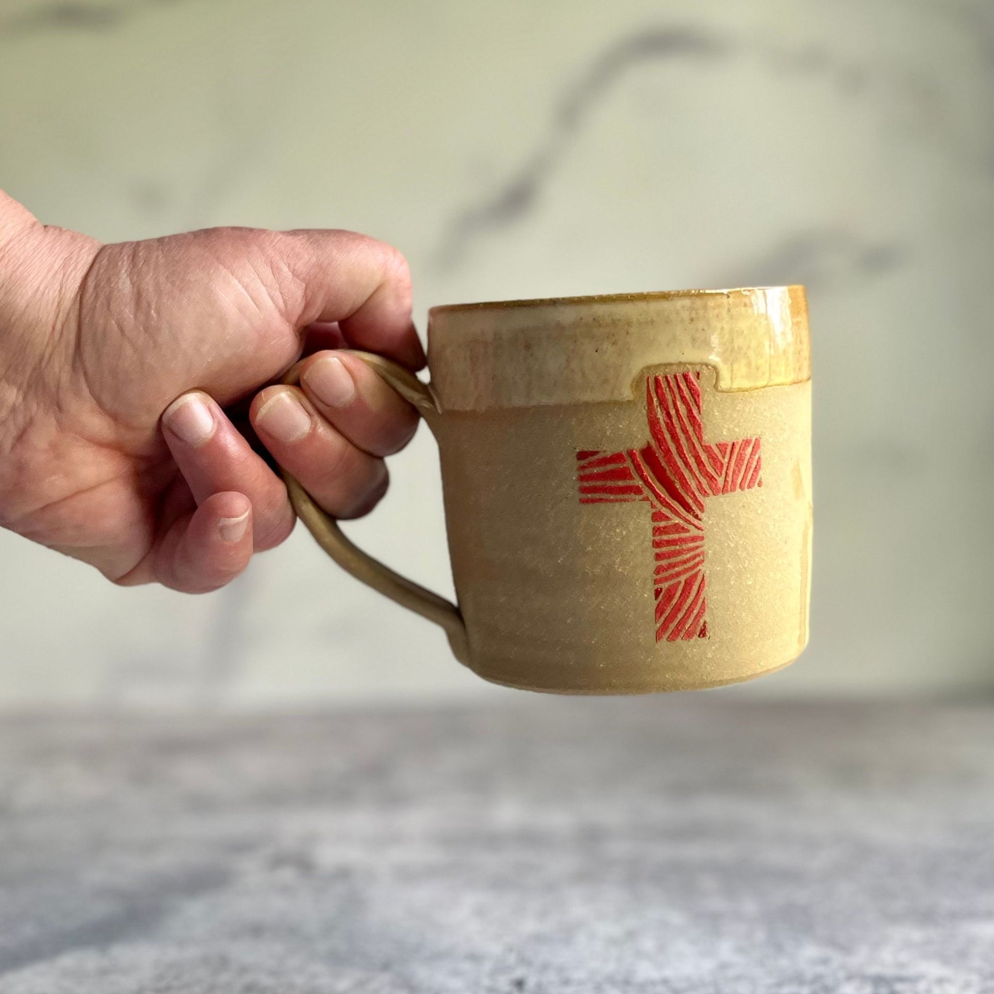 Hand holding a ceramic mug with a red abstract design on a blurred background